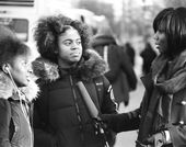Two young women in coats face a woman holding a microphone