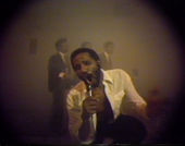 Grainy video still of artist Ulysses Jenkins singing into a microphone