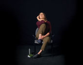 A woman sitting in an office chair holding her right knee up to her chest and her right hand to her face
