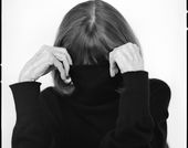 A black and white photo portrait of writer Joan Didion using her turtle-neck sweater to cover her face